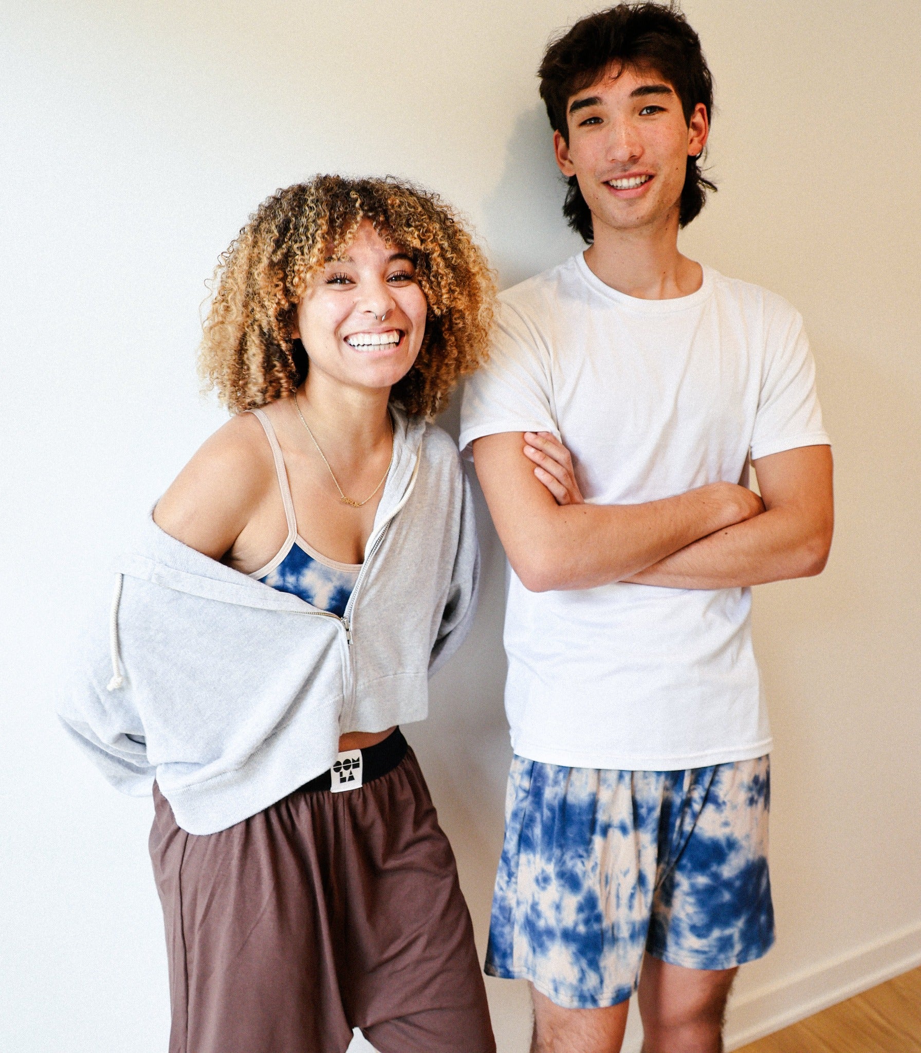 two smiling people, one wearing the featured shorts with their arms crossed, another wearing the matching bra