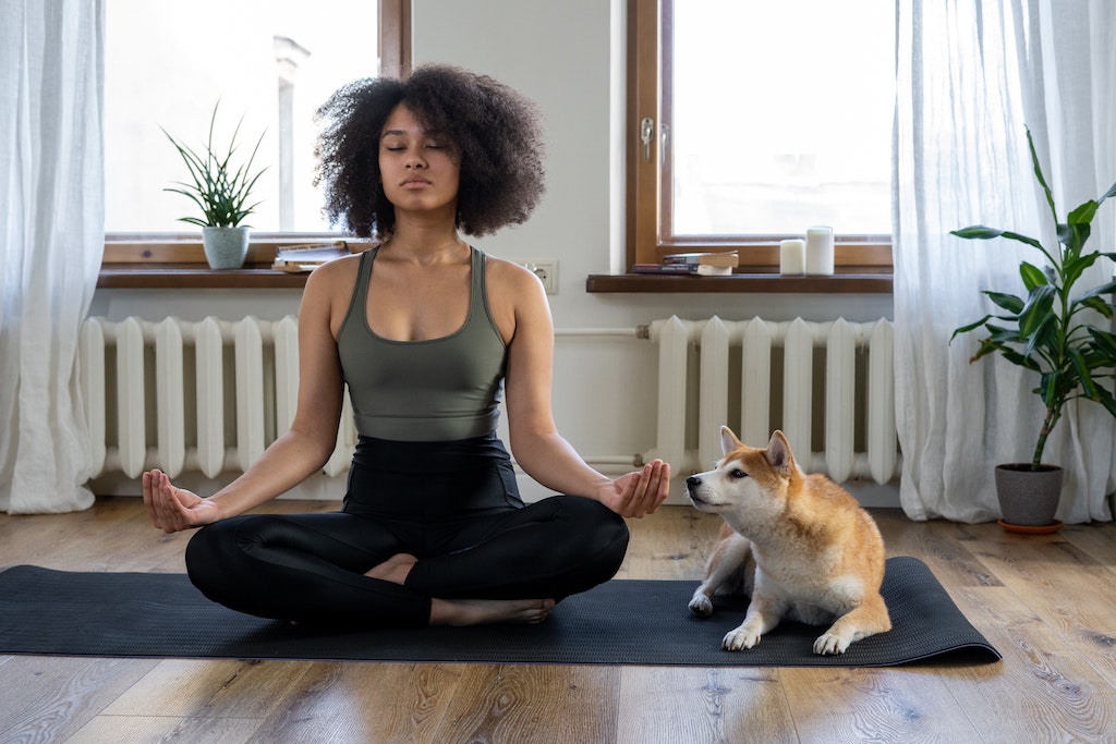 Woman meditating on a yoga mat with dog next to her