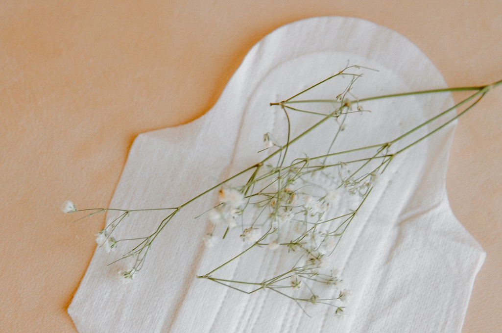 opened period pad with white flowers laying on it, on a tan background