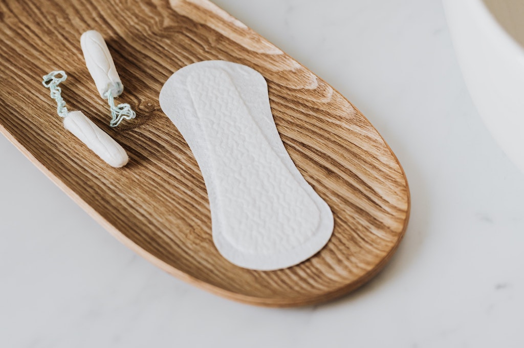 opened pad and tampons on a wooden dish on bathroom counter