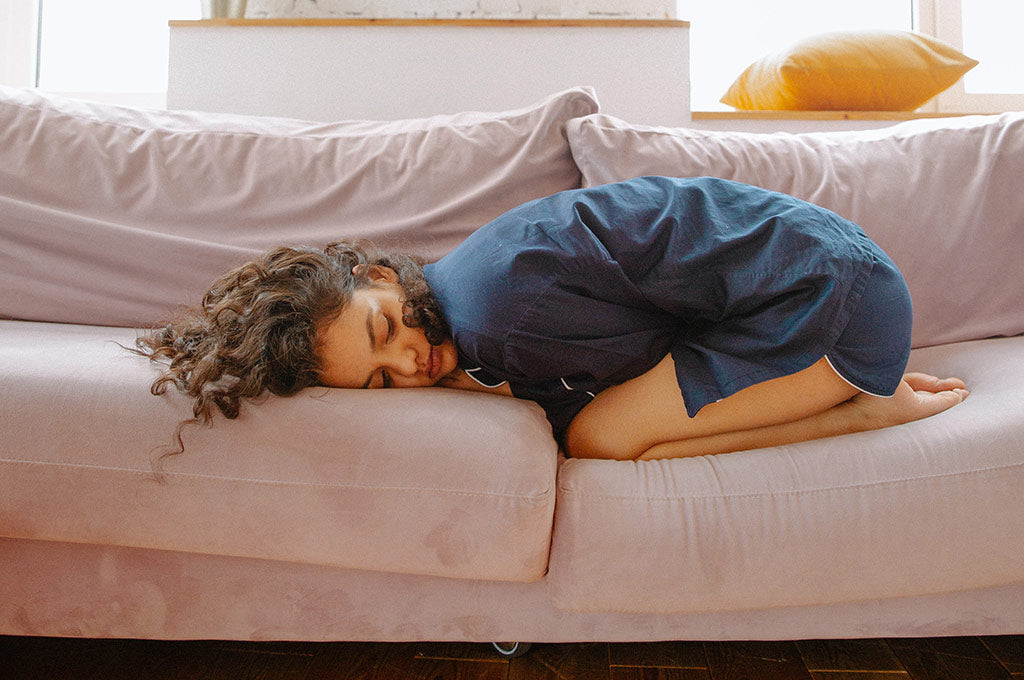 girl in pajamas curled up on couch, indicating period cramps