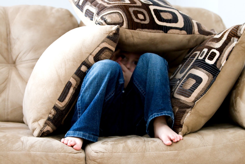 boy sitting on couch hiding under pillows